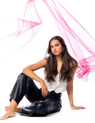a young woman in leather pants sitting on the floor with pink smoke.