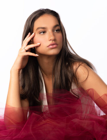 a young woman in a red tulle skirt posing on a white background.