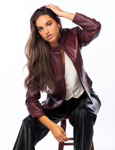 a woman in a burgundy leather jacket posing on a stool.