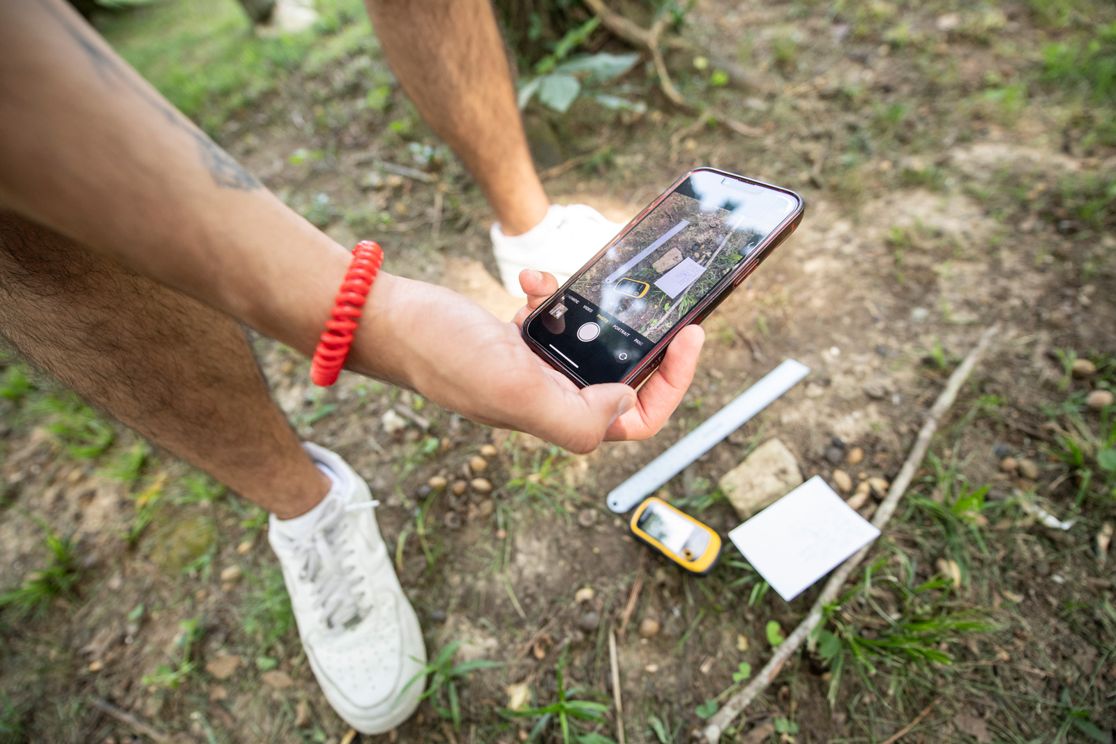 A person holding a cell phone in the woods.