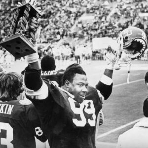 A black and white photo of a football player holding a trophy.