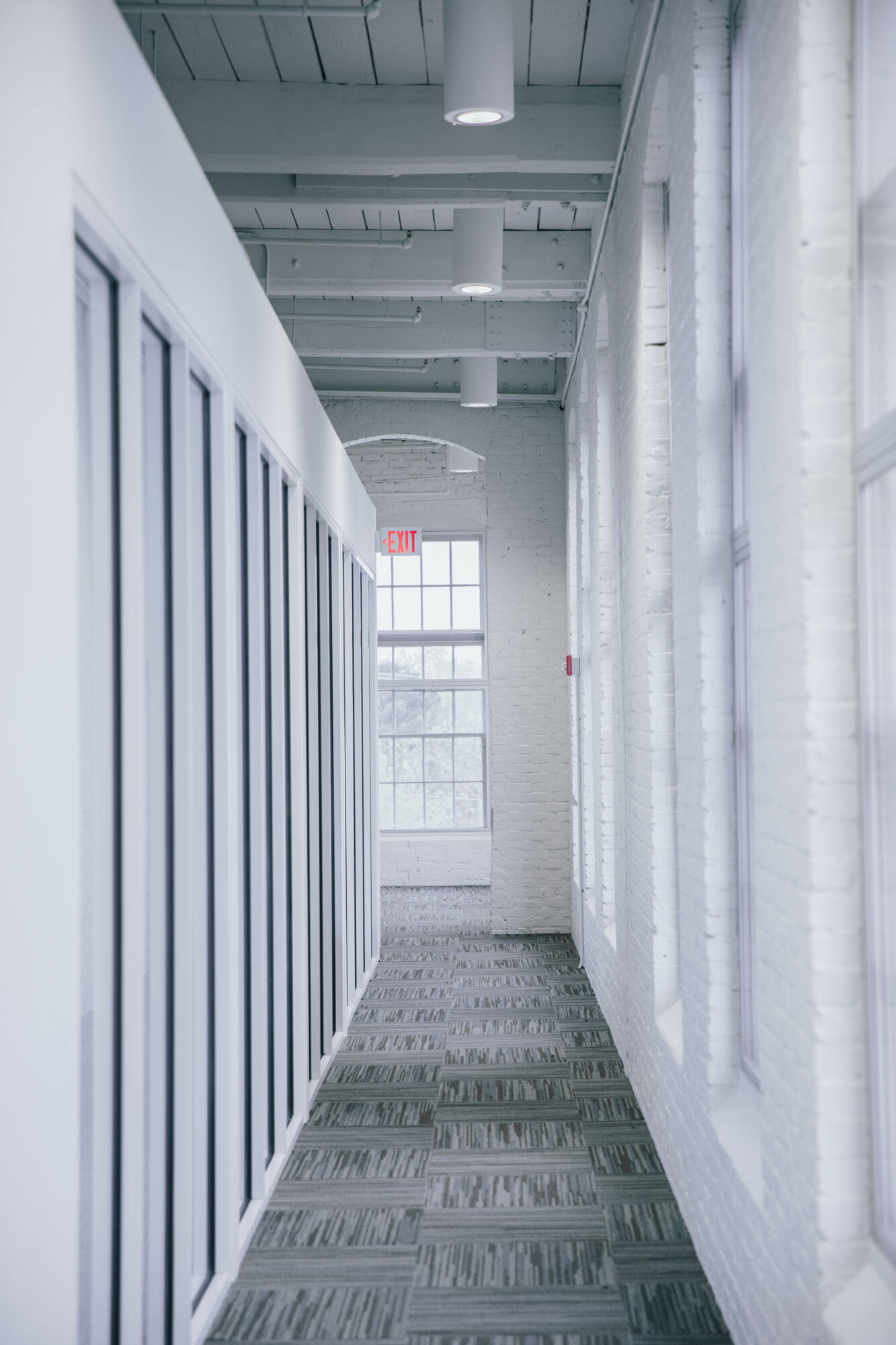 A hallway in an office with white walls and gray carpet.