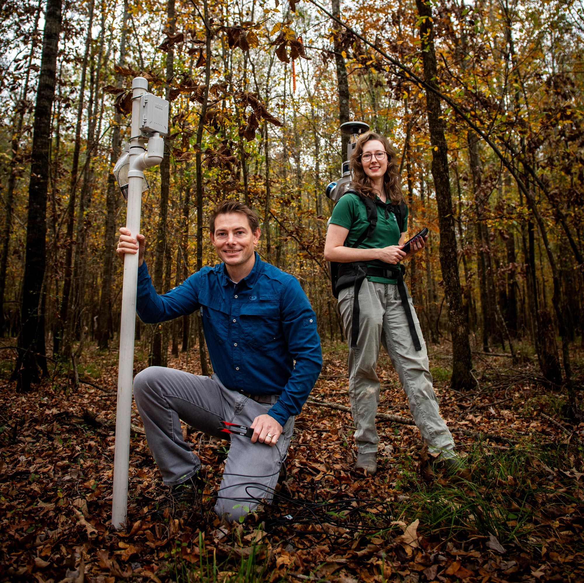 Two people standing in the woods with a pole.
