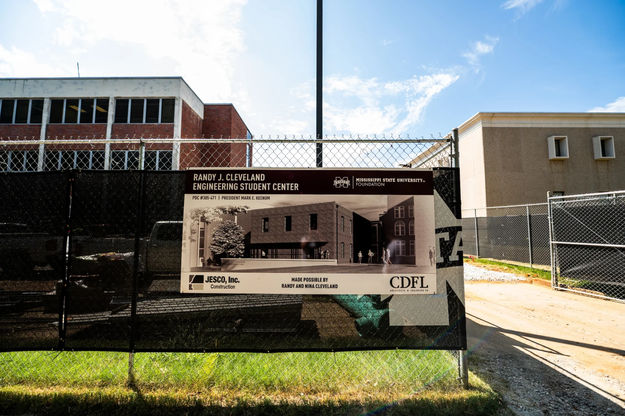 Sign on a chain-link fence for the Randy J. Cleveland Engineering Student Center construction project, with adjacent buildings visible.