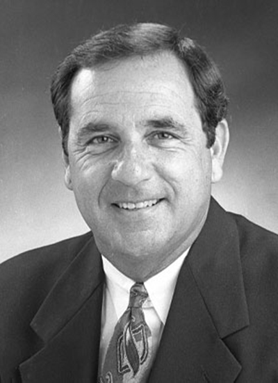 Black and white portrait of a man in a suit and tie, smiling at the camera.