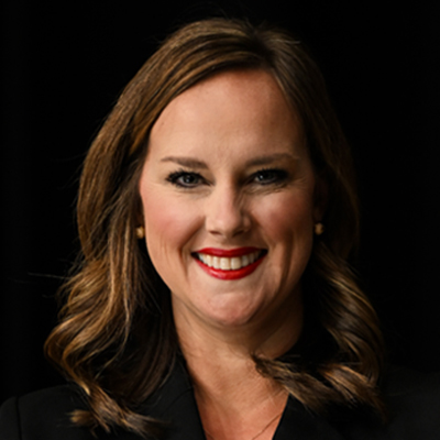 A woman with long brown hair and red lipstick smiles at the camera against a black background.