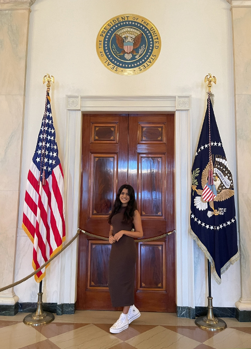 A person stands in front of a wooden door, flanked by the U.S. and presidential flags, under the Seal of the President of the United States.