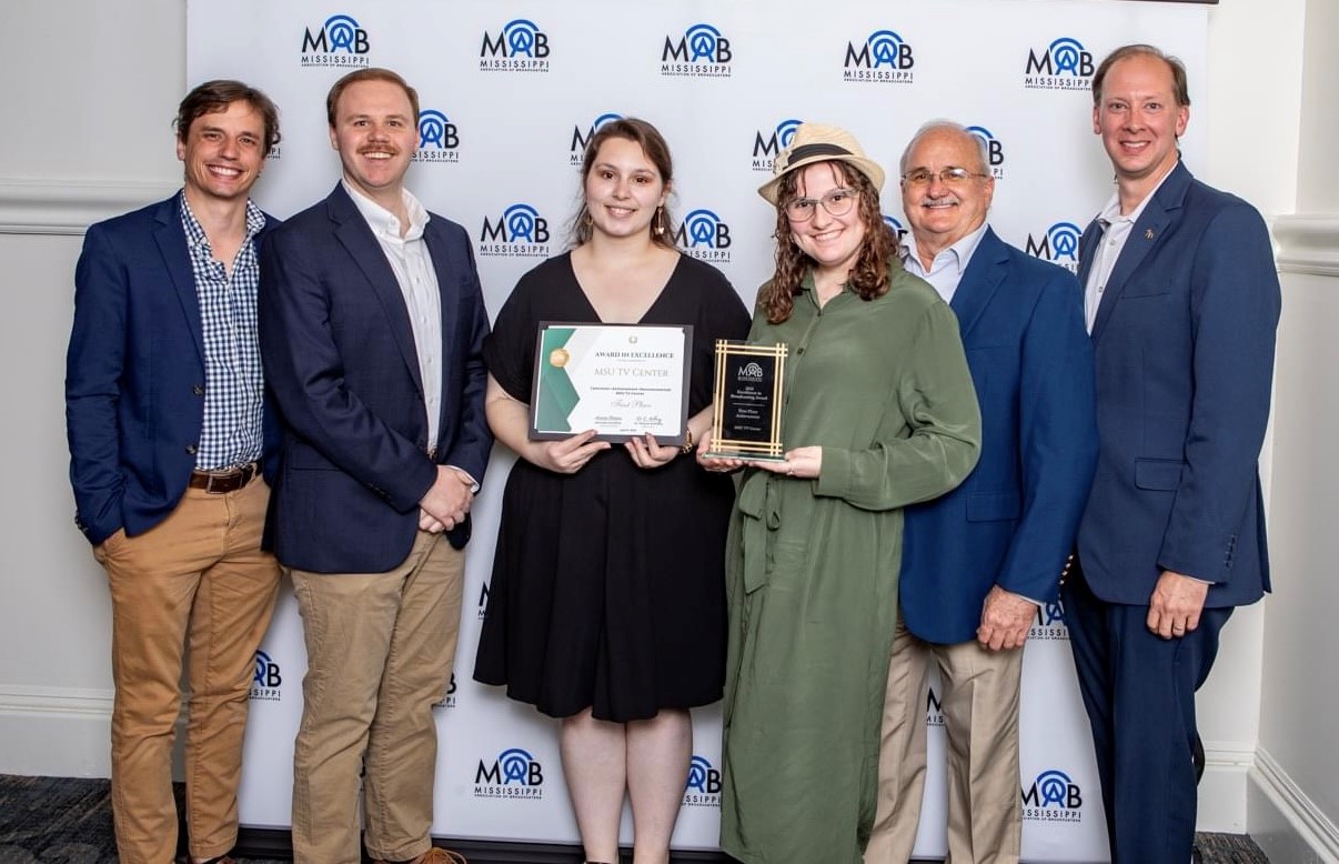 Six people standing in front of a backdrop, two holding awards.