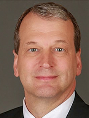 Portrait of a man in a suit, with short hair and neutral expression, set against a plain background.