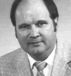 Black and white headshot of a man wearing a light-colored suit and tie, with short hair and a neutral expression.