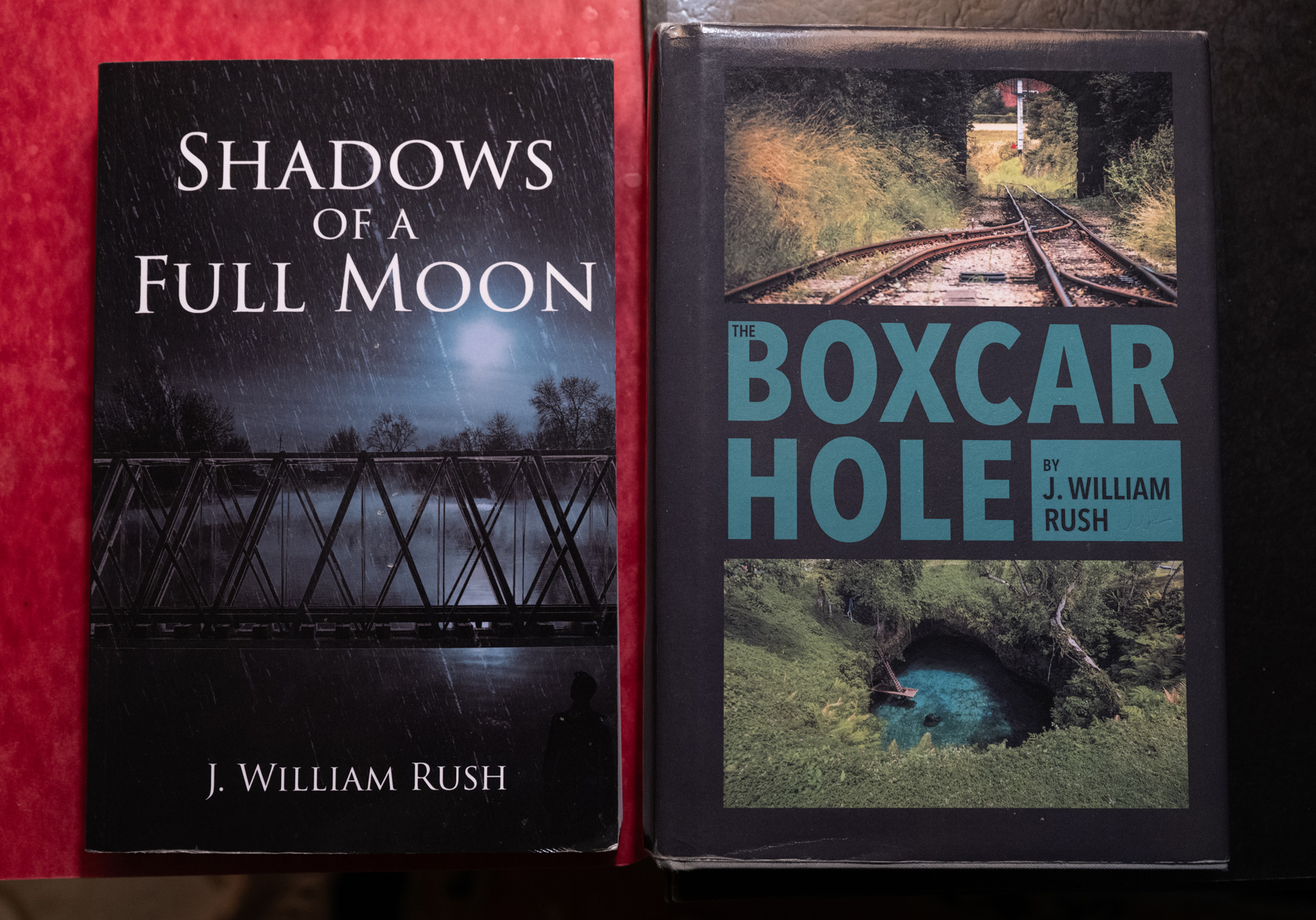 Two books by J. William Rush: "Shadows of a Full Moon" with a bridge at night on the cover, and "The Boxcar Hole" featuring train tracks and a water-filled hole.