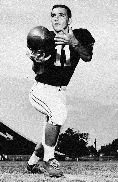 A football player wearing a number 11 jersey catches a football while posing on a field.