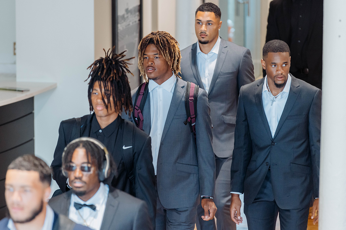 A group of men in suits, some with backpacks, walking in a hallway.