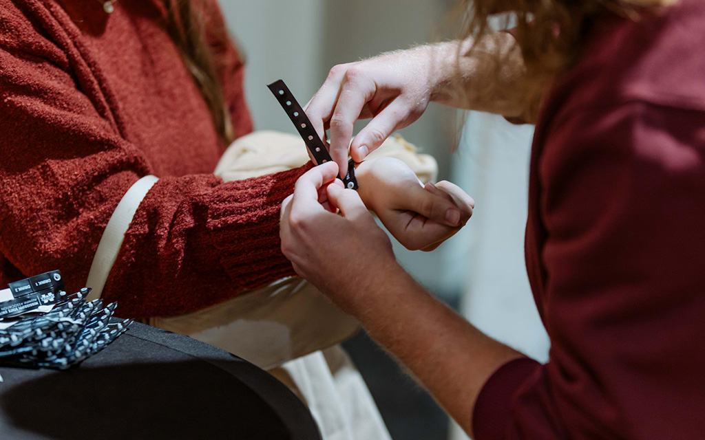 A person puts a black wristband on another person's wrist at what appears to be an event check-in or registration desk.
