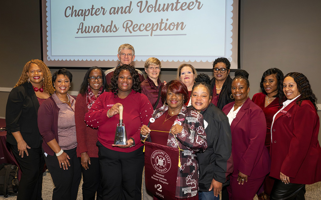 A group of people pose indoors at a Chapter and Volunteer Awards Reception, with one person holding a trophy and another holding a banner.