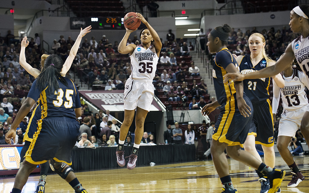 A Mississippi State basketball player jumps to take a shot while defended by opposing players during a game in a crowded indoor arena.