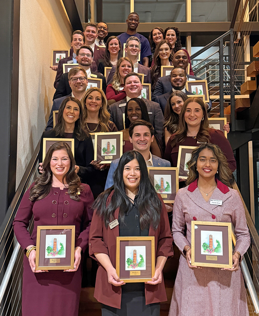 A group of people stands on a staircase, each holding a framed picture and smiling at the camera.