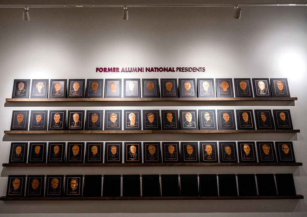 A wall display of engraved plaques features portraits of former alumni national presidents, arranged in three horizontal rows under a sign.