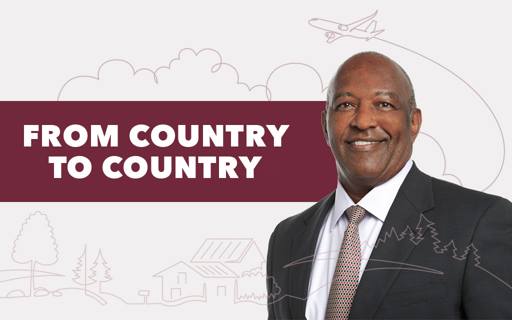 Smiling man in a suit stands beside bold text reading "From Country to Country," with simple line art of nature, buildings, and an airplane in the background.