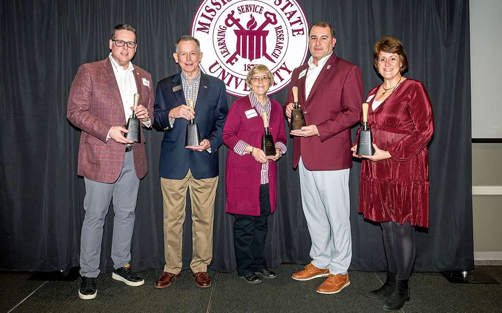 Five adults stand in front of a Mississippi State University backdrop, each holding a trophy-shaped award and posing for a group photo.