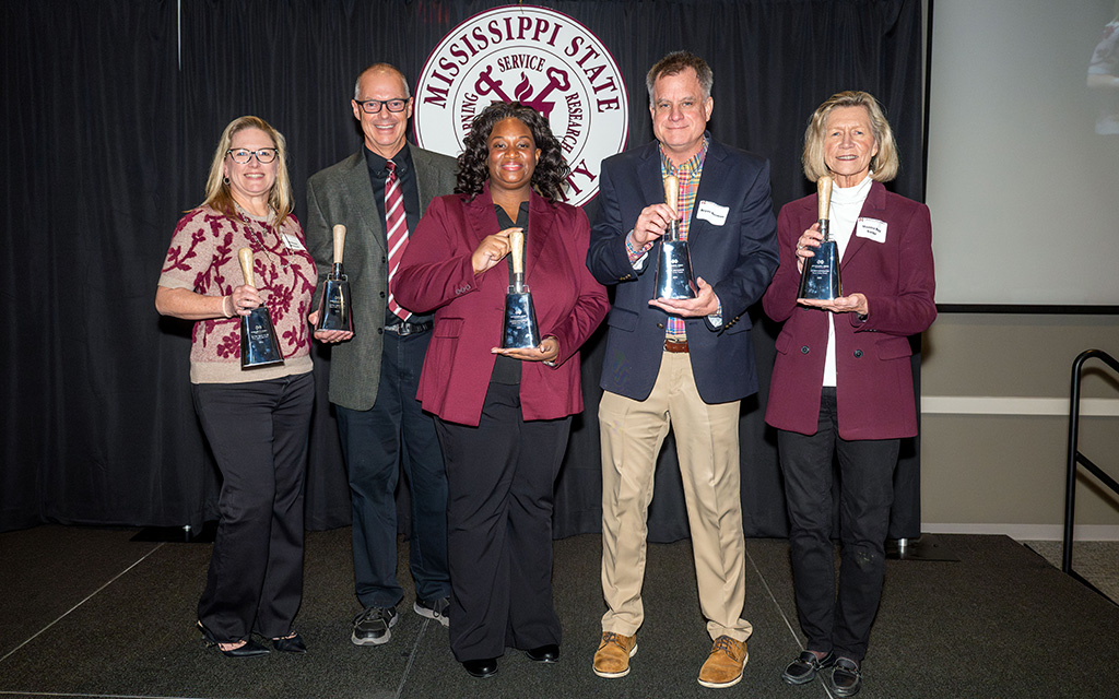 Five people stand in front of a Mississippi State University backdrop, each holding a glass award and posing for a group photo.