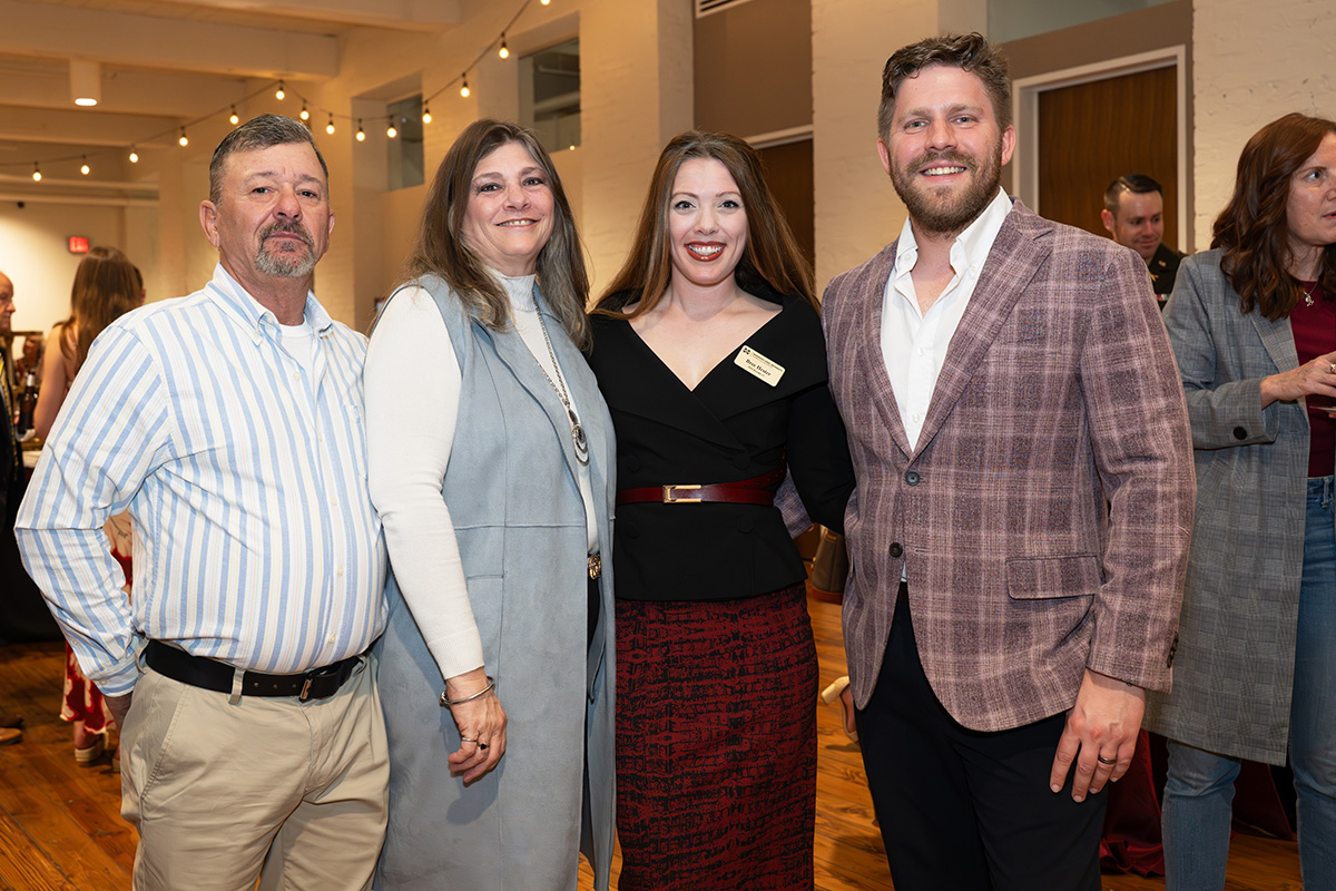 Four adults stand together and smile for a photo at an indoor event, dressed in business casual attire.