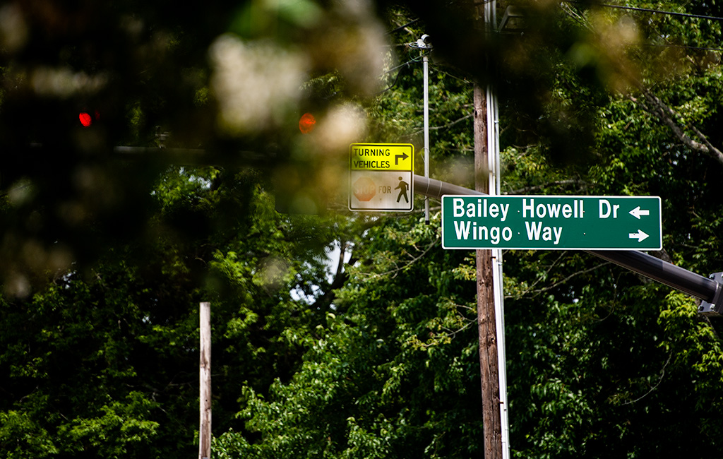 Street signs showing directions to Bailey Howell Dr and Wingo Way, with a traffic signal and trees in the background.