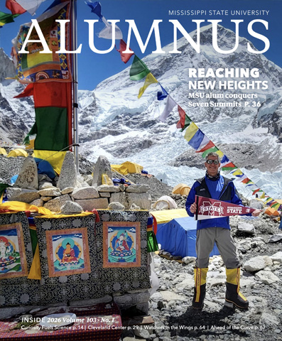 A person in climbing gear stands on a snowy mountain with prayer flags, holding a Mississippi State banner. Magazine cover text highlights climbing achievement by an MSU alumnus.