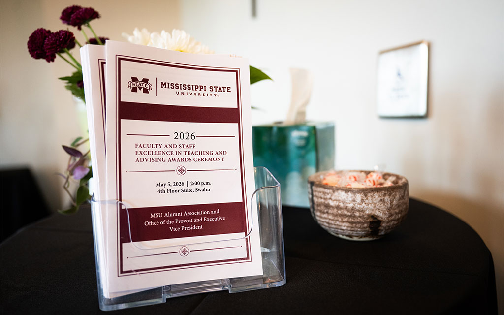 A pamphlet for the 2026 Mississippi State University Faculty and Staff Excellence in Teaching and Advising Awards Ceremony sits on a table with flowers and a tissue box.