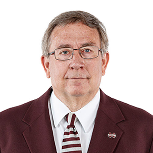 Man wearing glasses, a maroon suit jacket, and a striped tie, posing against a plain white background.