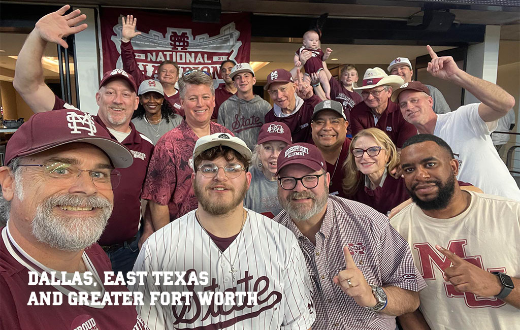 Group of people in Mississippi State apparel pose for a photo indoors, smiling and making hand signs, with a banner in the background. Text reads: “Dallas, East Texas and Greater Fort Worth.”.