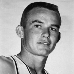 A young man with short hair is wearing a sleeveless sports jersey and looking slightly to the side against a plain background.