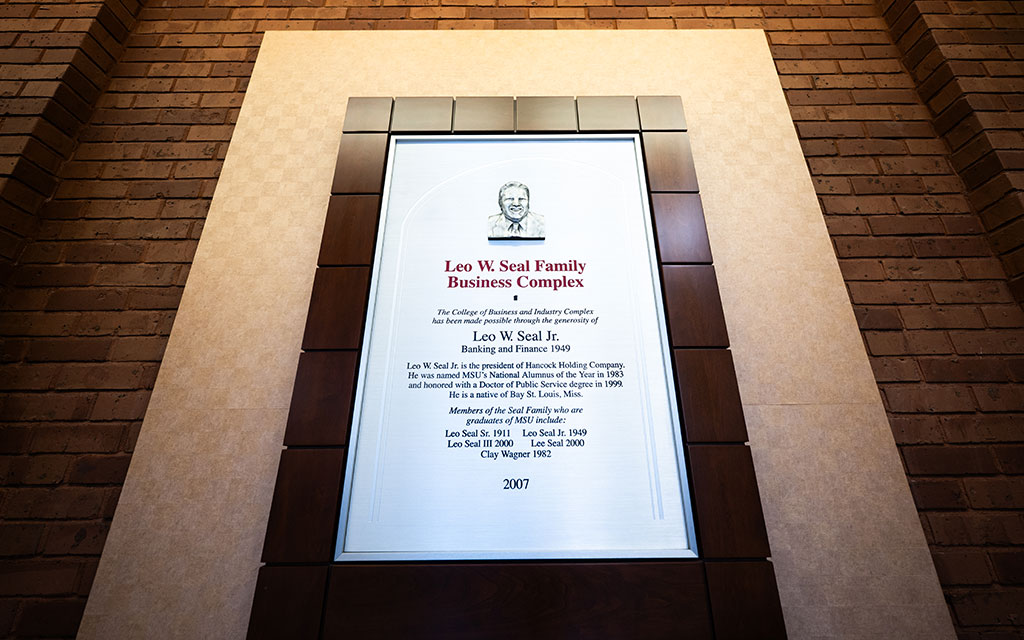 Plaque on a brick wall honoring Leo W. Seal Sr., detailing his achievements and family members, displayed at the Leo W. Seal Family Business Complex, dated 2007.