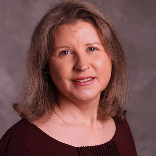 Woman with shoulder-length brown hair wearing a maroon top, smiling slightly, in front of a neutral gray background.