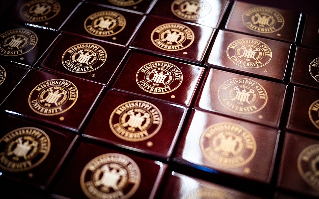 Rows of maroon boxes with gold Mississippi State University seals are closely arranged side by side.