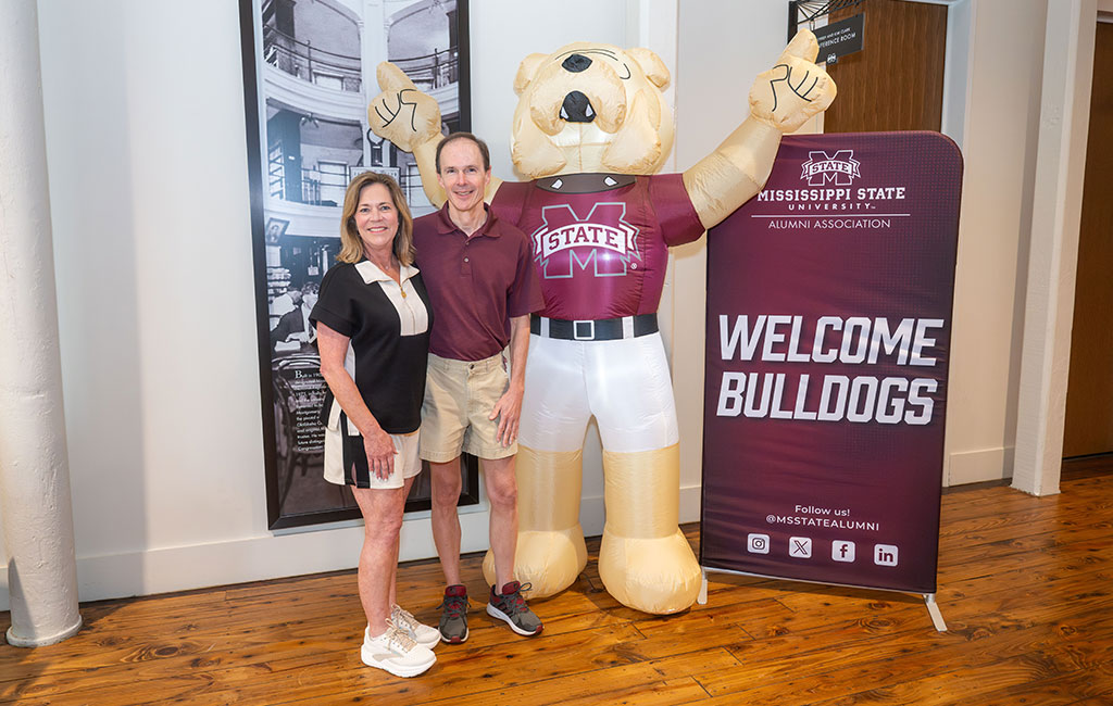 Two people stand next to an inflatable bulldog mascot and a “Welcome Bulldogs” sign at a Mississippi State University event.