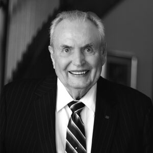 Elderly man in a pinstripe suit and striped tie, smiling at the camera in a black and white photo.